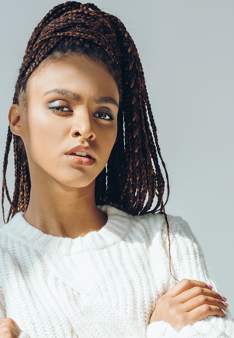Woman with braids in cozy sweater, serious expression.