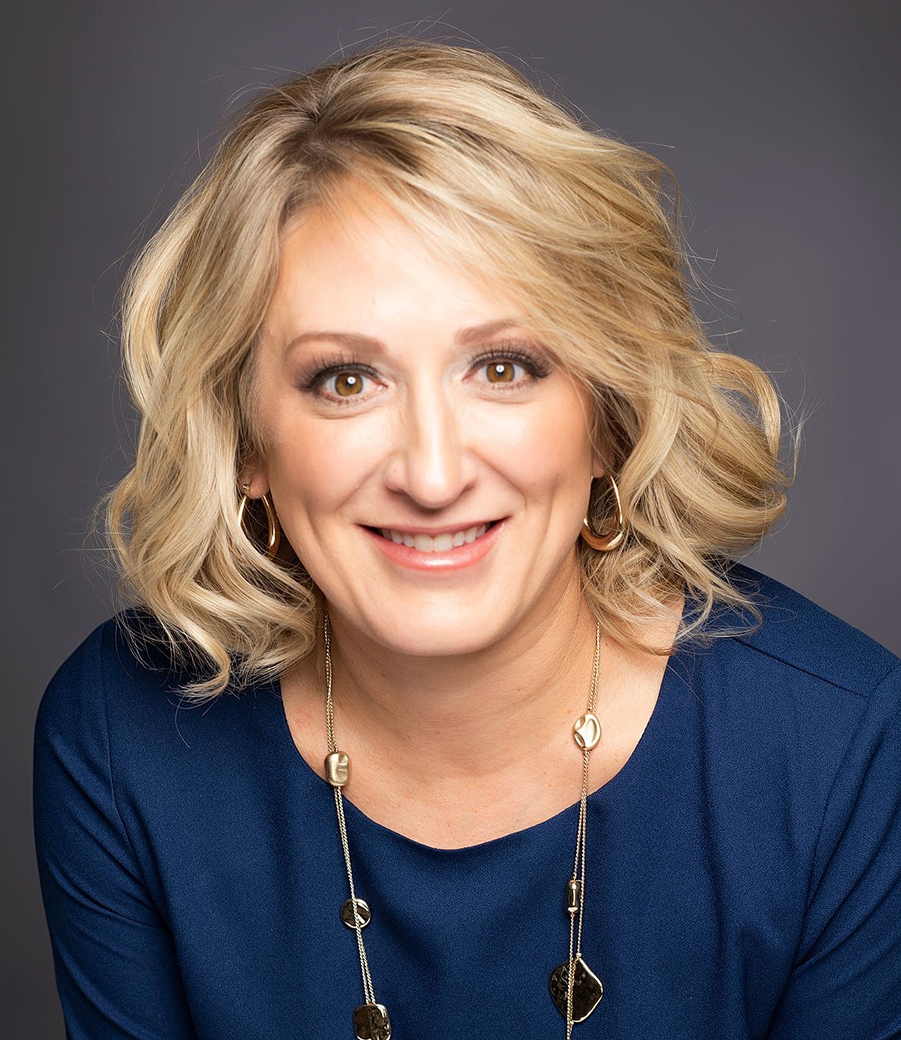 Smiling woman with blonde curly hair and necklace.