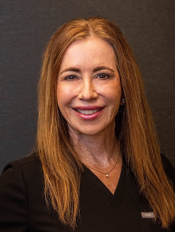 Smiling woman in professional attire against dark background.