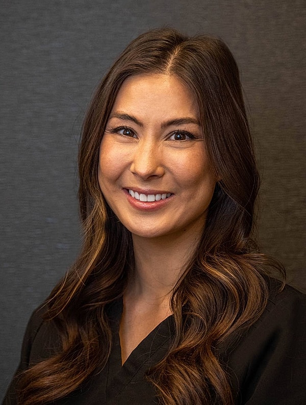 Smiling woman in medical attire against gray background.