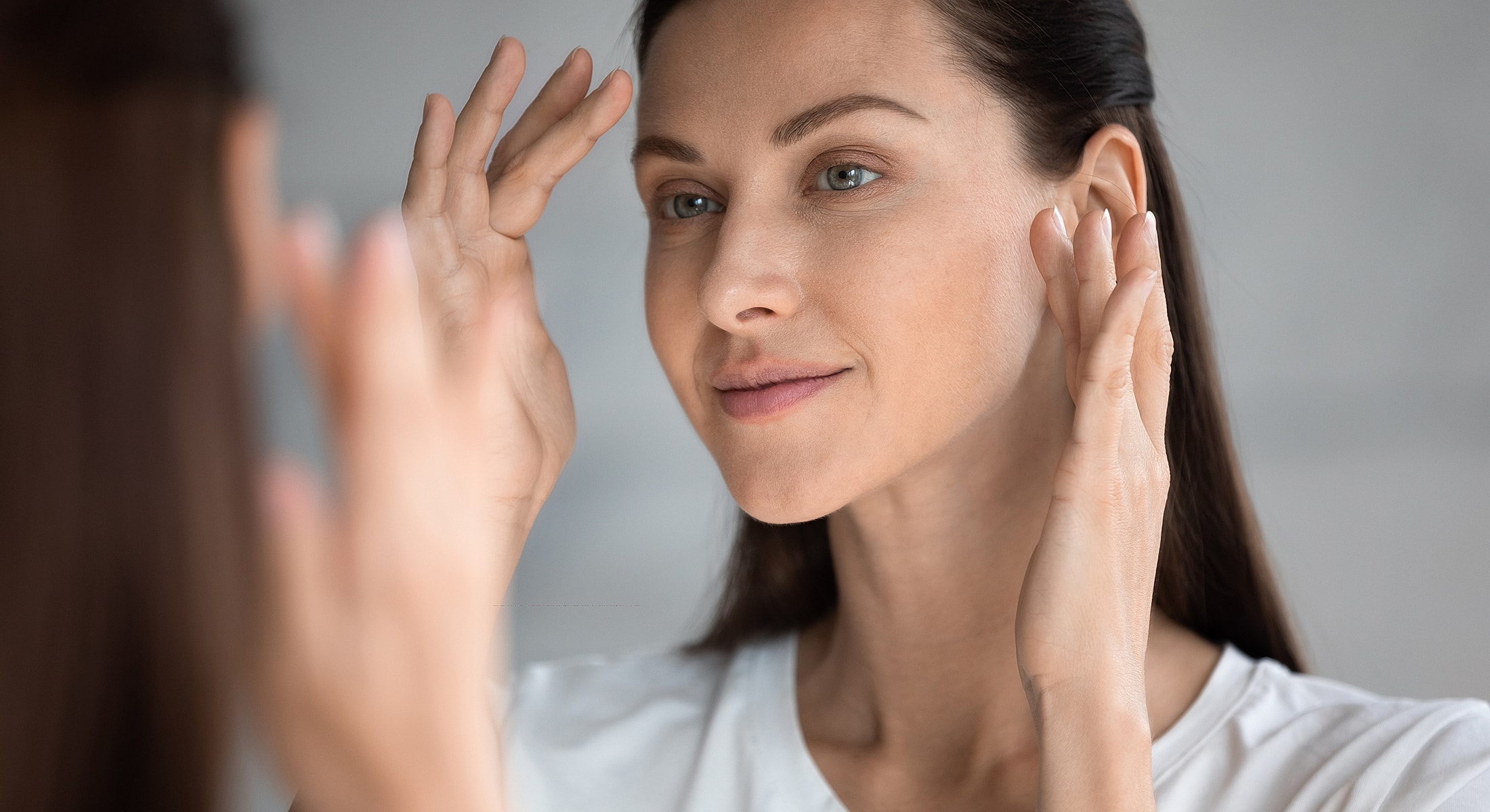 Woman applying skincare in front of a mirror.